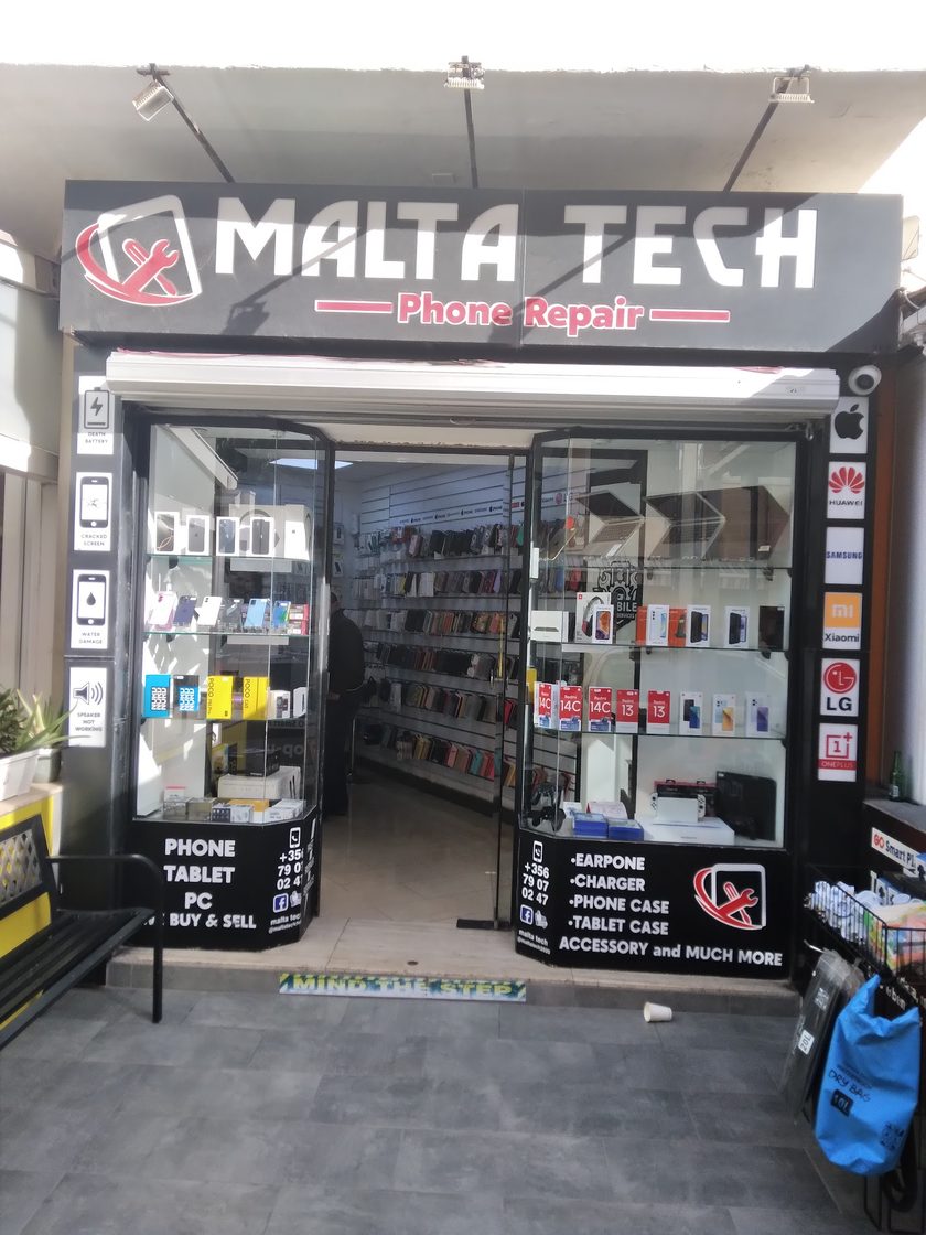 The shopfront under the Malta Tech Phone Repair sign, with fault symbols down the left of the doorway and Apple, Huawei, Samsung, Xiaomi, LG and OnePlus logos down the right. A member of staff stands inside the doorway, turned away from the camera
