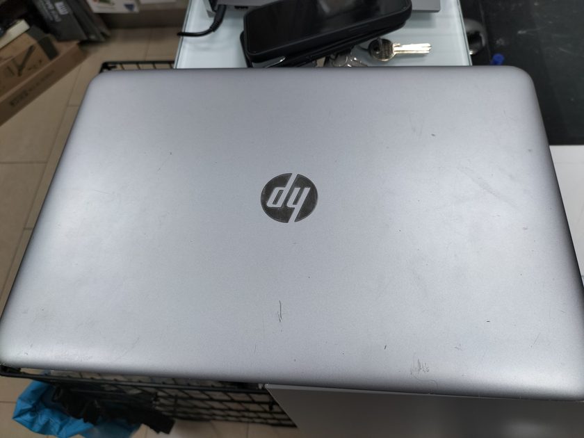 A closed HP laptop on the shop counter, with a phone case, keys and stacked stock boxes on the shelving behind it