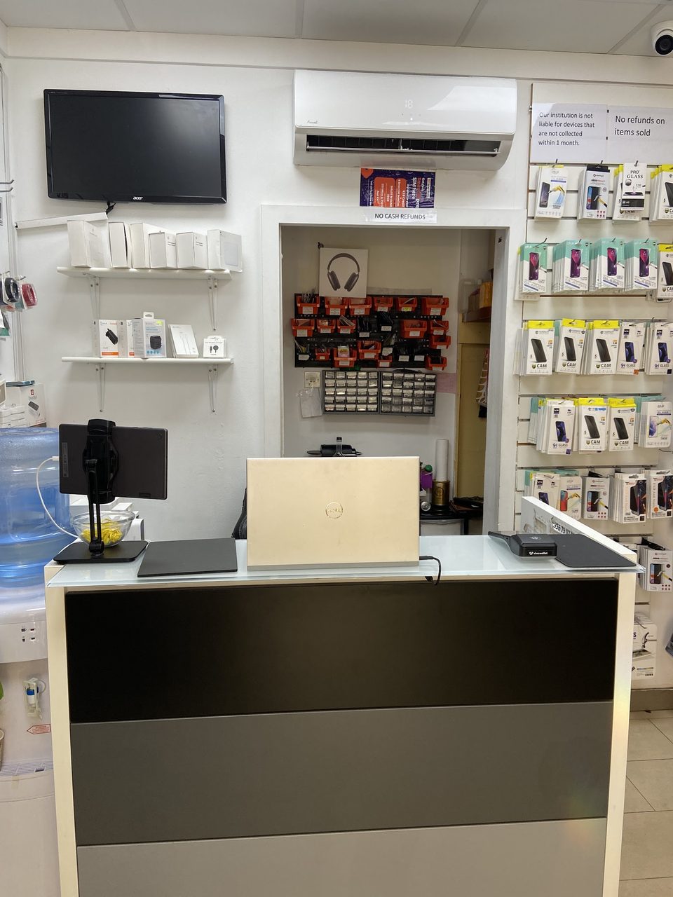 The service counter from the shop floor, with the repair bench and its parts drawers through the doorway behind, and tempered glass screen protectors hung on the right hand wall