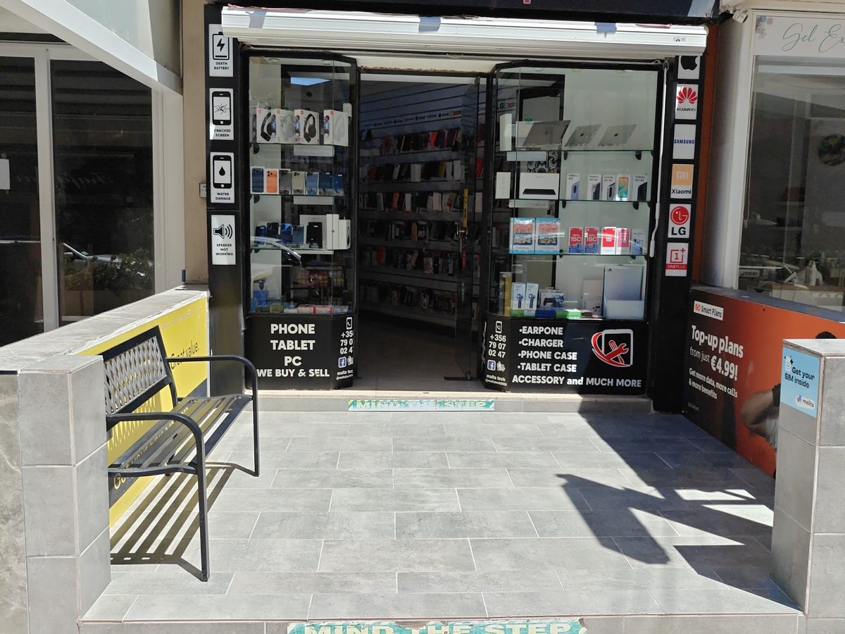 The Malta Tech shopfront on Triq il-Maskli seen from the pavement, with a bench beside the door and a mind the step tile across the threshold